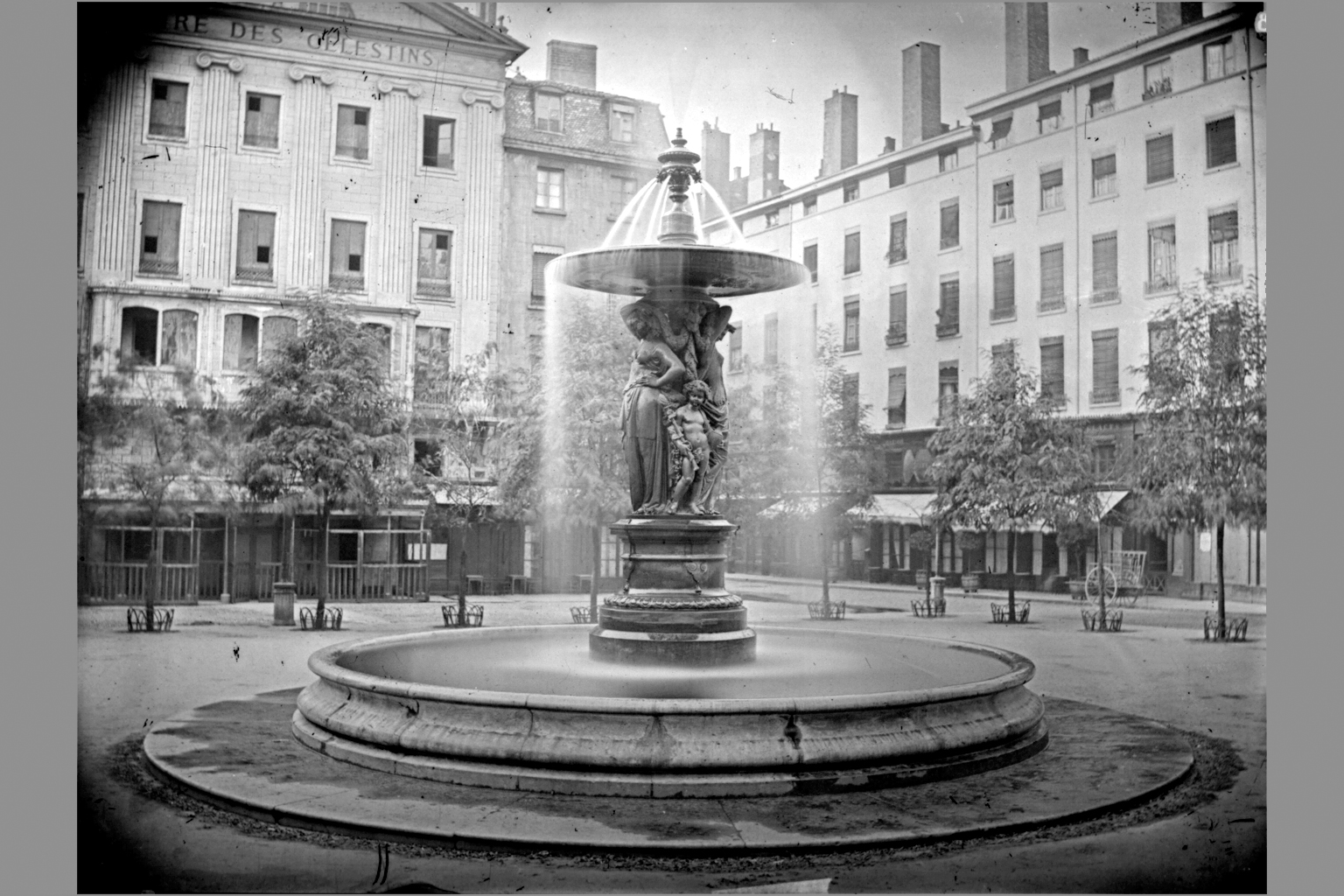 Fontaine sur la place des Célestins installée par la Compagnie des Eaux en 1858, avec l'ancien théâtre en arrière-plan, photographie négative sur plaque de verre, cliché du service de la voirie (cote : 3PH/610)