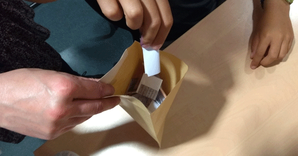 Photo représentant des mains d'enfants et d'adultes mettant des papiers dans une enveloppe