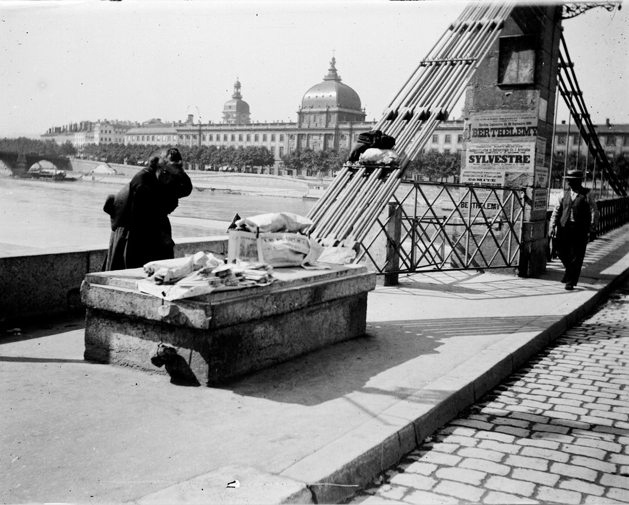 Vendeuse de journaux à l'entrée du pont de l'Hôtel-Dieu : photo négative NB sur plaque de verre (vers 1900, cote : 10PH/149)