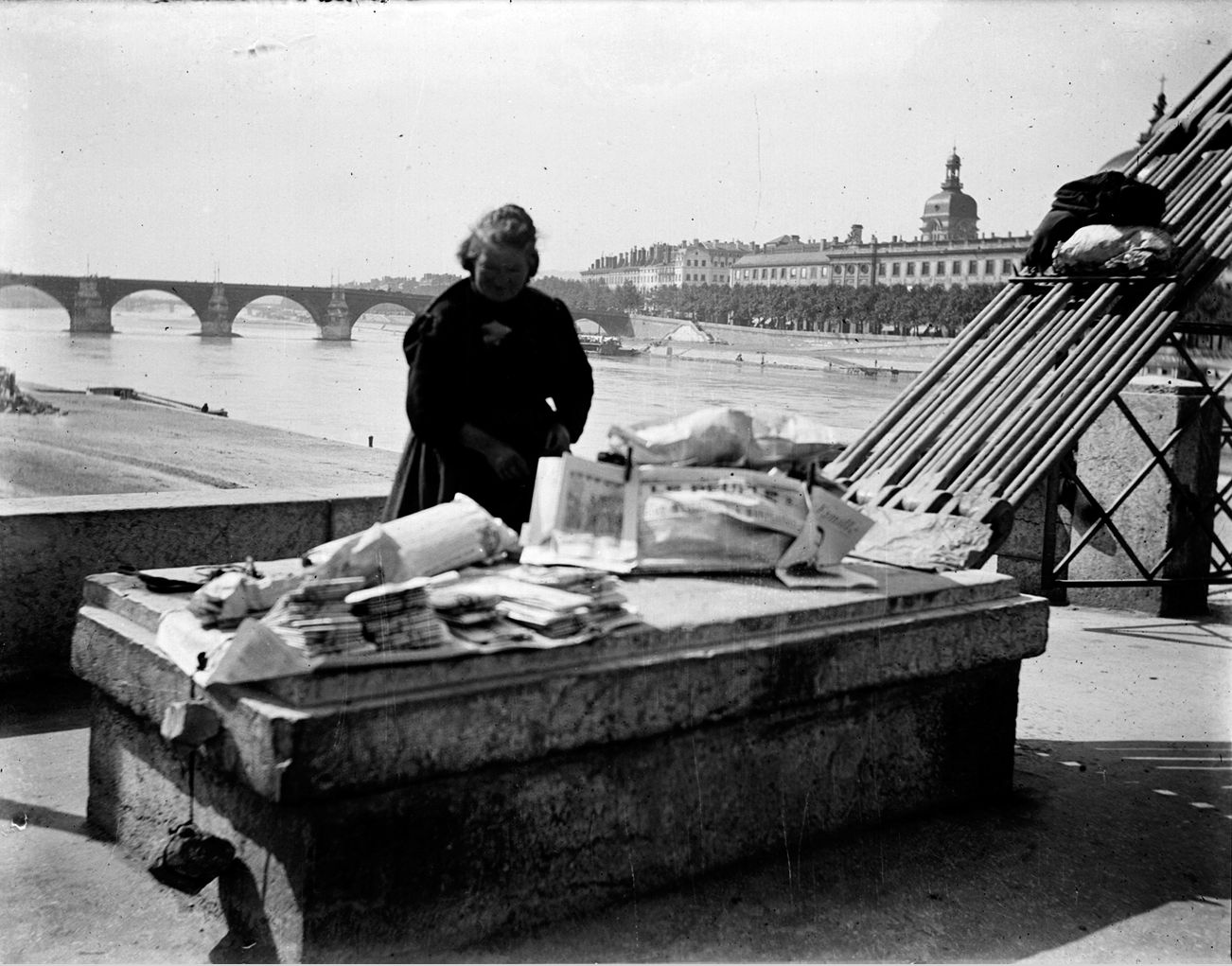 Vendeuse de journaux à l'entrée du pont de l'Hôtel-Dieu : photo négative NB sur plaque de verre (vers 1900, cote : 10PH/151)