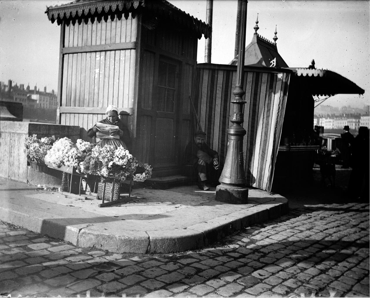 Marchande à fleurs à l'entrée d'un pont : photo négative NB sur plaque de verre au gélatino-bromure d'argent (vers 1900, cote : 10PH/61)