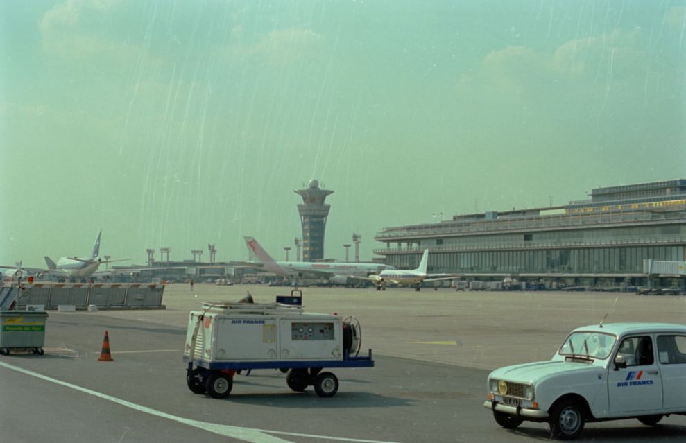 Aéroport de Lyon-Satolas, avions et véhicules terrestres devant les bâtiments : photo. couleur, auteur anonyme (1980-1985, cote 38PH/130/3)